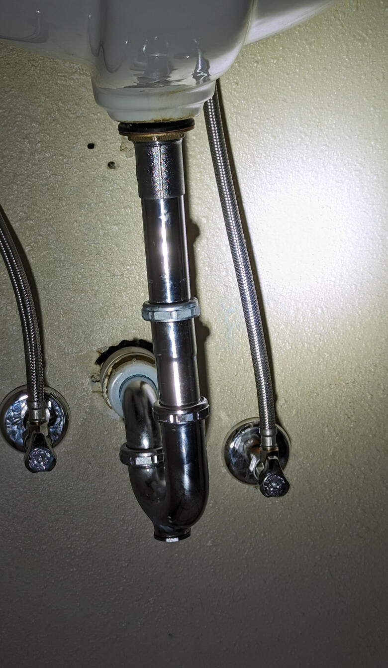 Under-sink plumbing with metal P-trap, drain pipe, and two flexible water supply lines connected to shut-off valves installed by Third Day Plumbing - Des Moines Iowa.