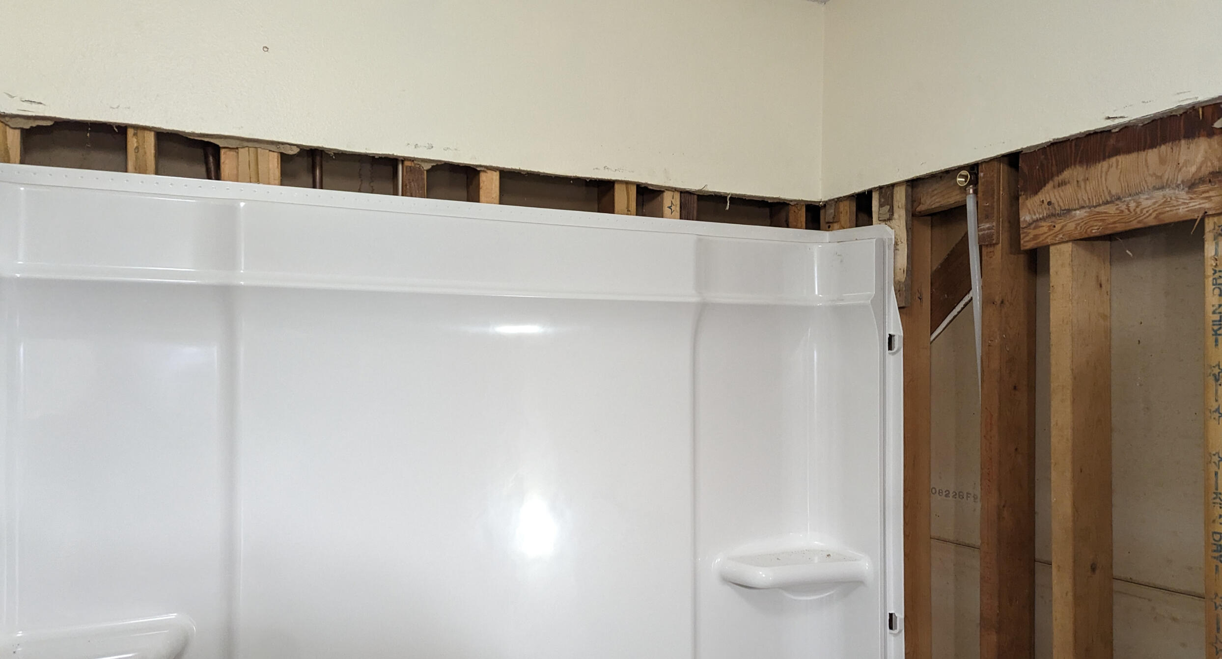 A partially installed bathroom tub surround with exposed wall studs above and to the side, showing an unfinished renovation.